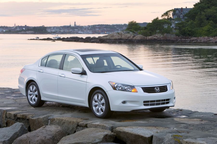 A white 2009 Honda Accord EX-L V6 midsize sedan model parked on rocks near a lake shore