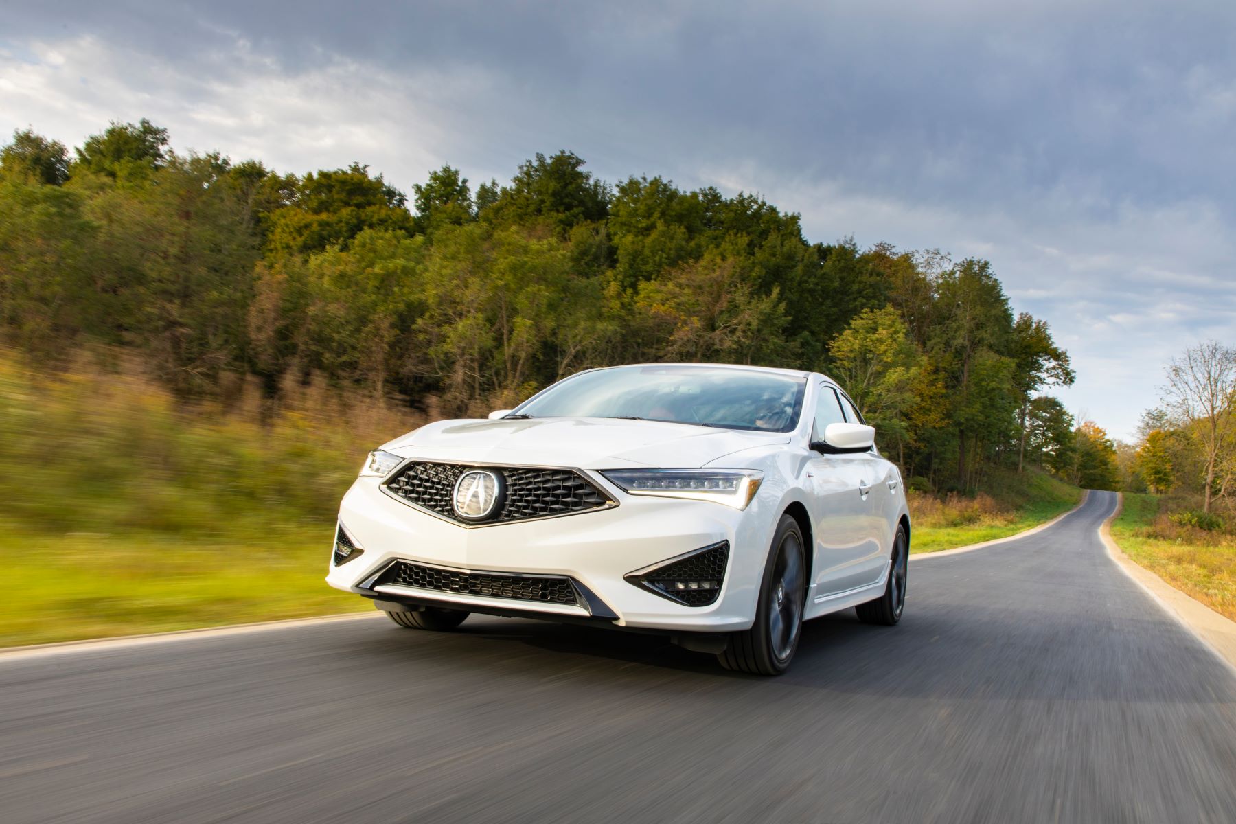 A white 2021 Acura ILX A-Spec compact executive luxury car model driving past a forest