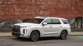 A white 2023 Hyundai Palisade midsize crossover SUV model parked on a street next to a red brick wall