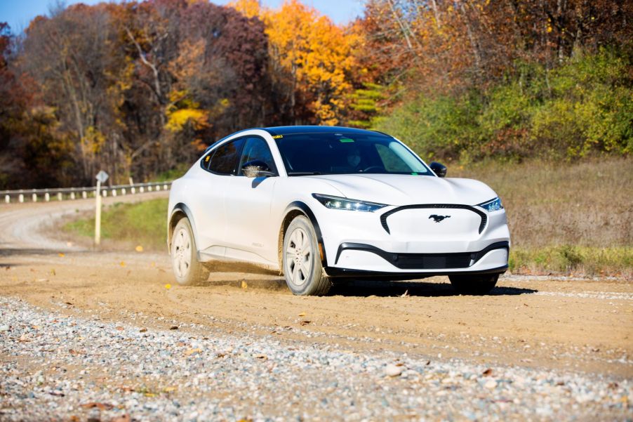 A white Ford Mustang Mach-E all-electric compact SUV model driving on a gravel road