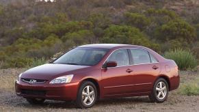 A dark red 2003 Honda Accord midsize sedan model parked on a dirt plain near forest hills. The 2003 model is one of the worst Honda Accord models.