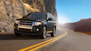 A 2009 Ford Escape compact crossover SUV model driving down a highway framed by rocky mountains