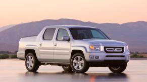 A silver-gray 2010 Honda Ridgeline RTL midsize pickup truck model parked on a wet asphalt lot in the wilderness