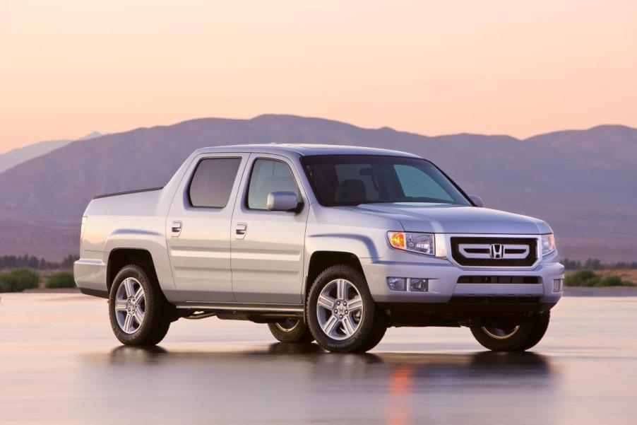 A silver-gray 2010 Honda Ridgeline RTL midsize pickup truck model parked on a wet asphalt lot in the wilderness