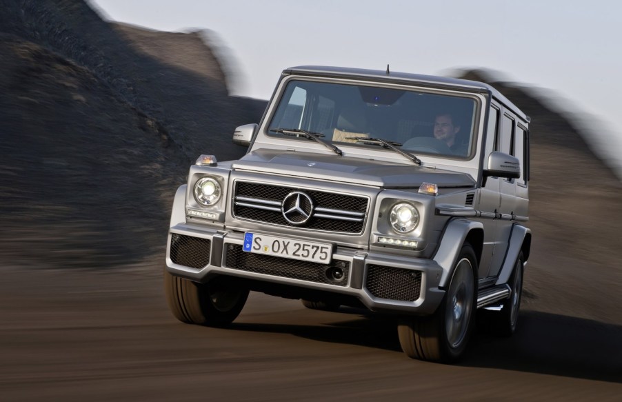 Advertising shot of a 2013 Mercedes G-Class SUV by AMG with a $56k MSRP price driving down a road, the background blurred behind it.