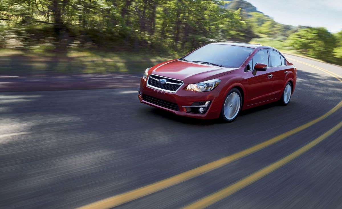 A read subaru drives down a road