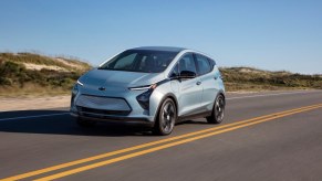 A blue Chevrolet Bolt EV electric car drives down a coastal road.