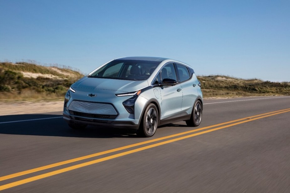 A blue Chevrolet Bolt EV electric car drives down a coastal road. 