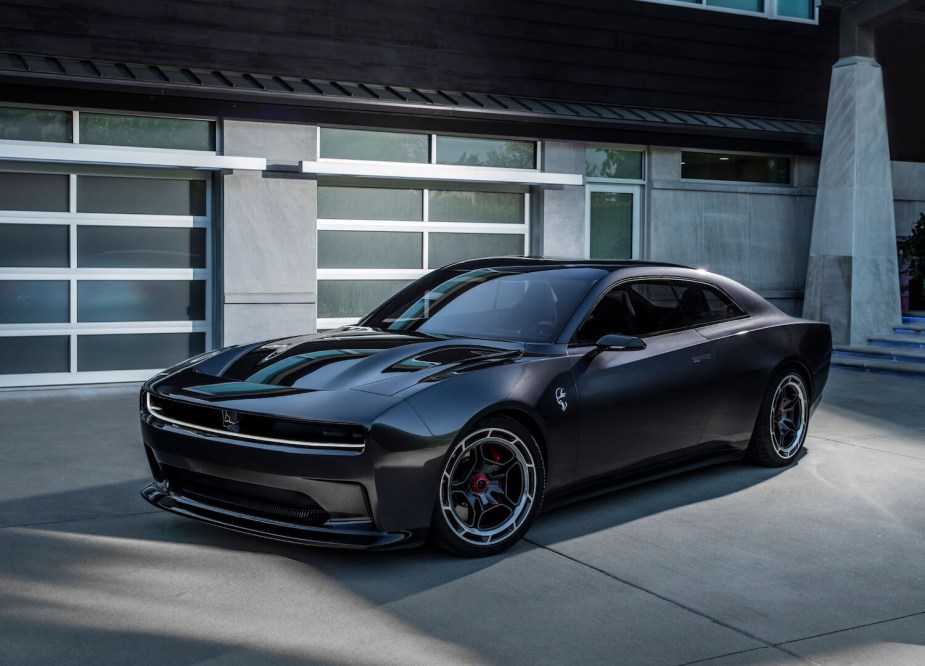 Promo photo of the gray 2024 electric Dodge Charger Daytona coupe prototype parked in front of a garage door.