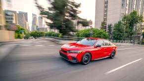 A red 2023 Honda Civic shows off its sports car design cues as it drives down a city street.