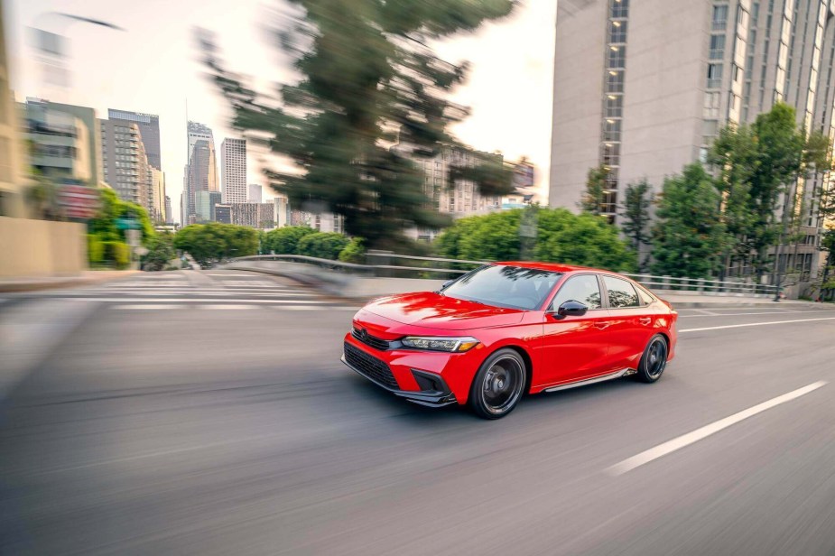 A red 2023 Honda Civic shows off its sports car design cues as it drives down a city street. 