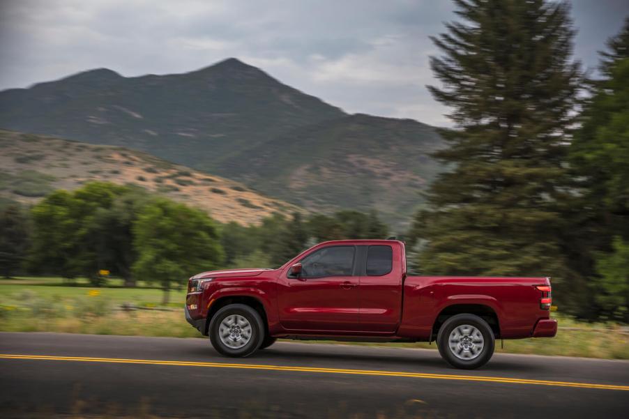 The profile view of a red midsize Nissan Titan pickup truck, driving in front of a mountain range.