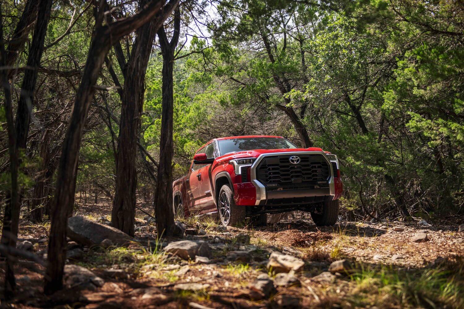 A red Toyota Tundra pickup truck shows off its off-road capability as it navigates a trail through the woods.