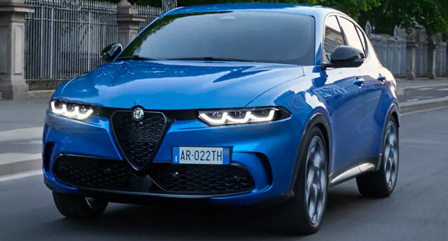 A blue 2023 Alfa Romeo Tonale small luxury plug-in hybrid SUV is driving on the road. 