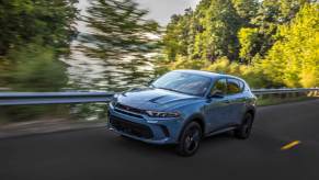 A blue-gray 2023 Dodge Hornet compact SUV model driving on a forest highway