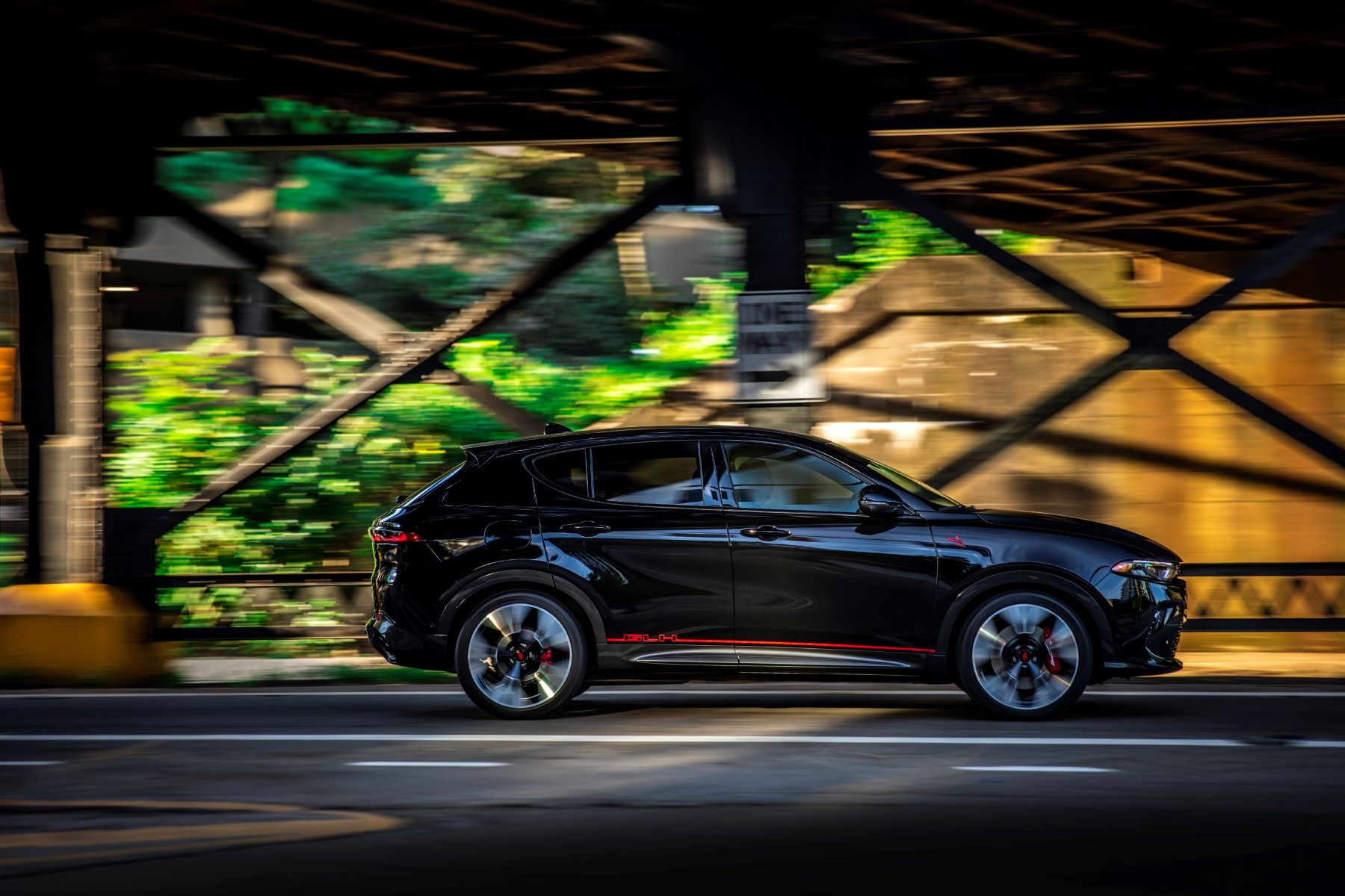 A side exterior profile shot of a 2023 Dodge Hornet plug-in hybrid (PHEV) compact SUV model driving under a bridge