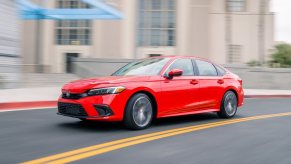 Honda's 2023 Civic in bright red compact car corners on a city street.