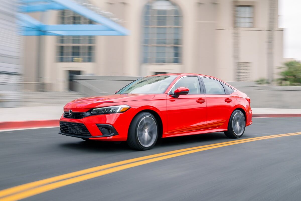 Honda's 2023 Civic in bright red compact car corners on a city street.