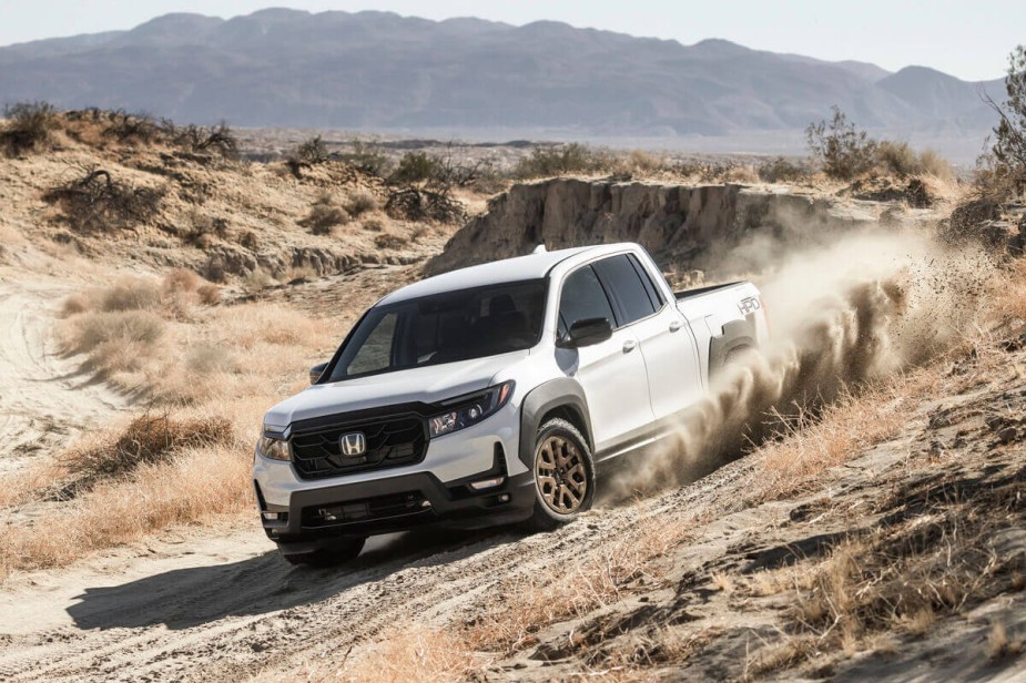 A white new 2023 Honda Ridgeline pickup blasts over a hill.