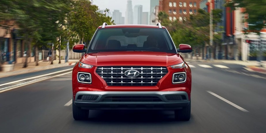 A red 2023 Hyundai Venue subcompact SUV is driving on the road. 