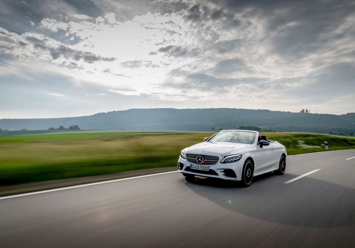 A white 2023 Mercedes-Benz C 300 Cabriolet drives down a road near a field