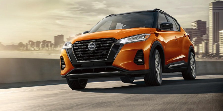 An orange Nissan Kicks subcompact SUV is driving on the road.