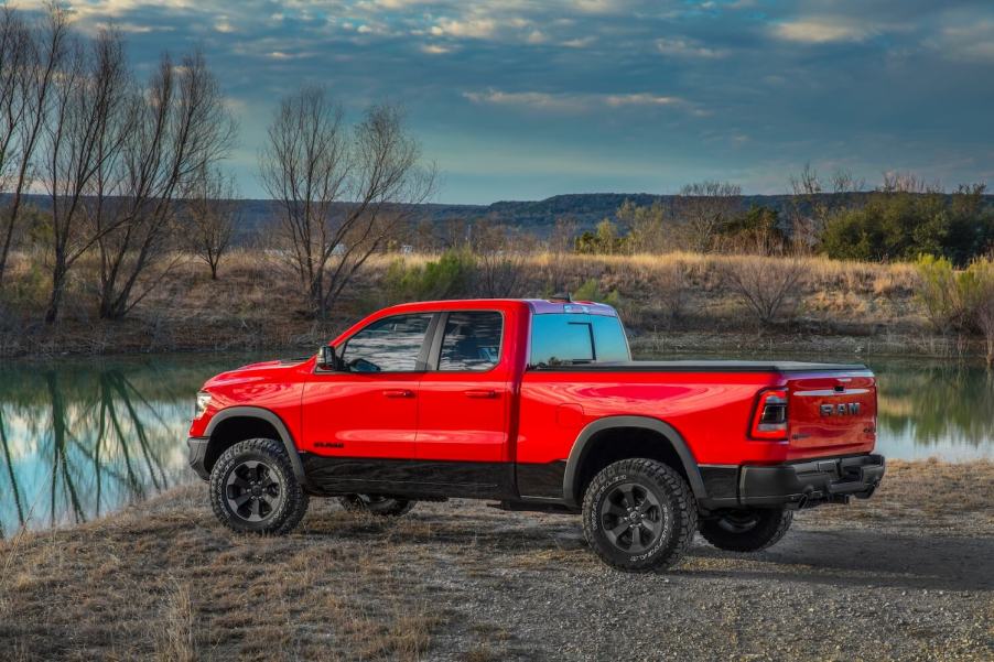 Promo photo of a bright red Ram 1500 with a cheap quad cab configuration parked by a lake.