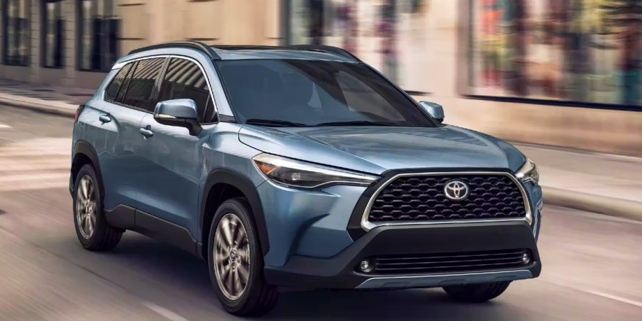 A blue 2023 Toyota Corolla Cross subcompact SUV is driving on the road. 