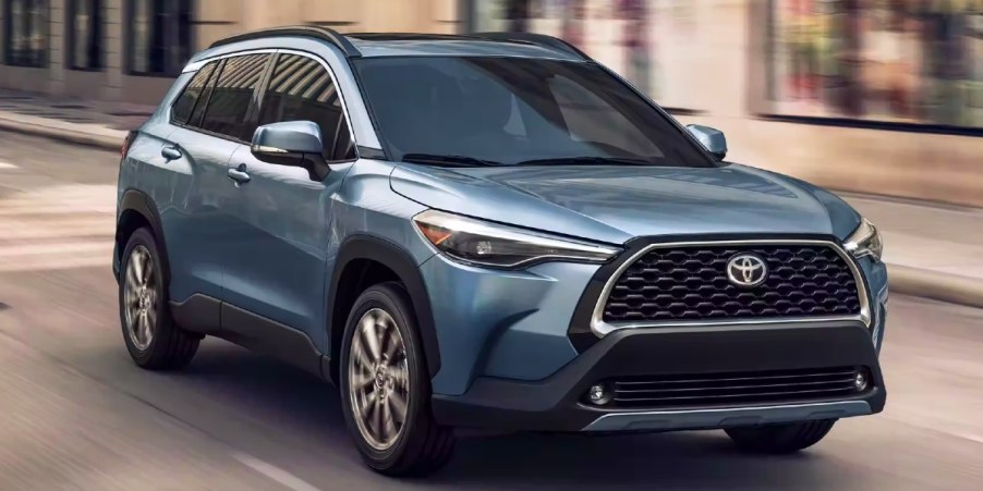 A blue 2023 Toyota Corolla Cross subcompact SUV is driving on the road.