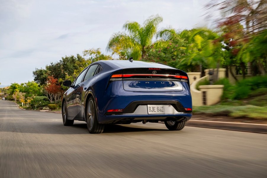 A new 2023 Toyota Prius shows off its blue color as it cruises down a country road.