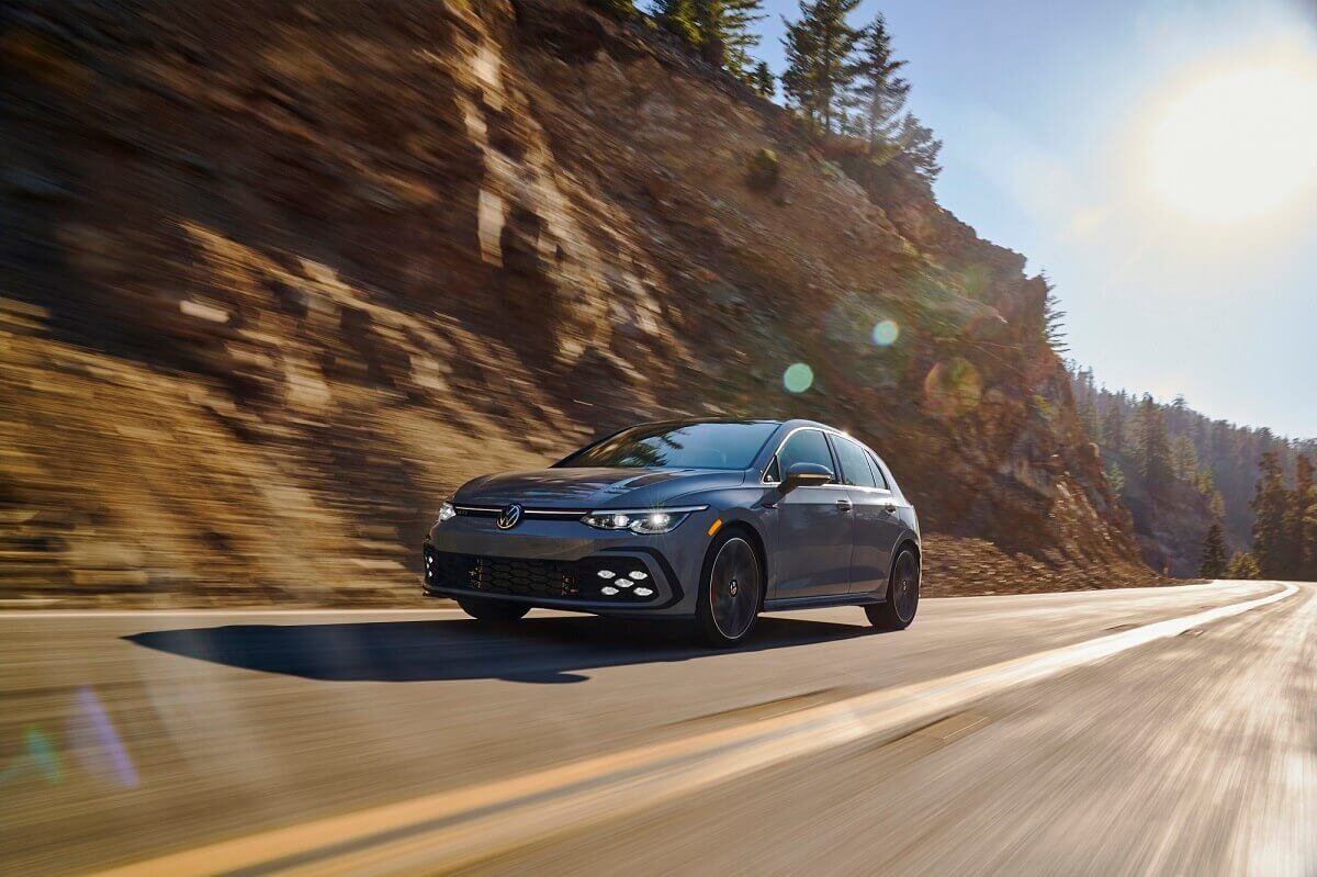 The 2023 Volkswagen Golf GTI shows off its sensible German hatchback car styling while it blasts down a mountain road.