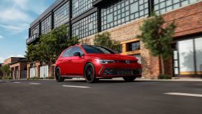 A red 2023 Volkswagen Golf GTI 40th Anniversary Edition shows off its celebratory German car paintwork and looks as it drives past an apartment building.