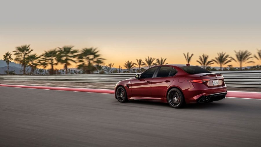 A red 2022 Alfa Romeo Giulia Quadrifoglio, like a Dodge Charger Hellcat, uses copious horsepower to attack a test track at sunset.