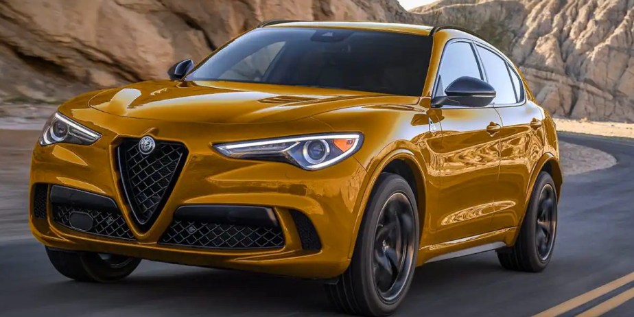 A yellow Alfa Romeo Stelvio Quadrifoglio small luxury performance SUV is driving on the road. 