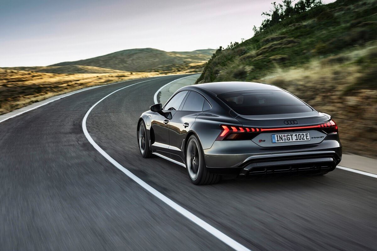 A gray Audi e-tron GT blasts down a country road with visible name plates.