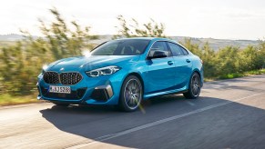 A new 2023 BMW 228i Gran Coupe drives down a coastal road in the sunlight.