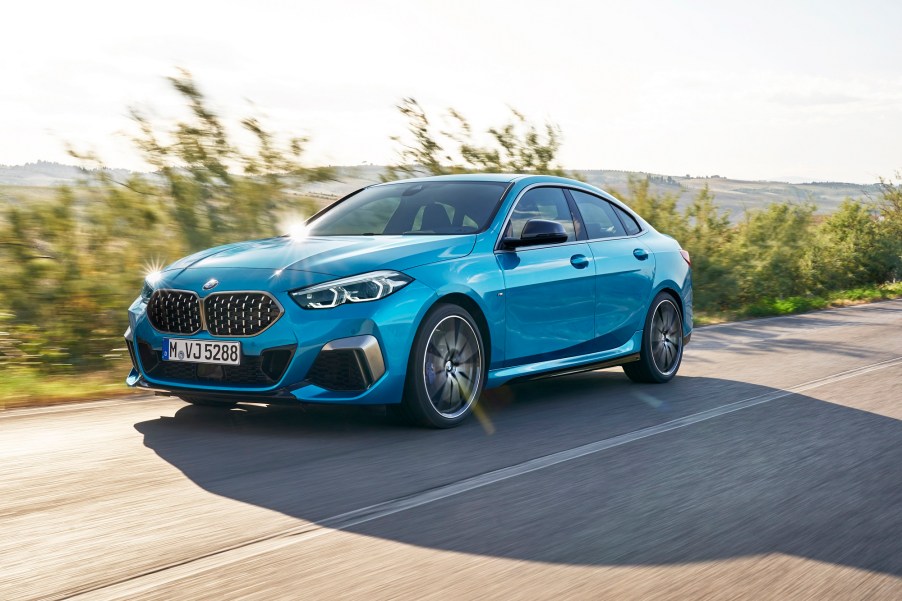 A new 2023 BMW 228i Gran Coupe drives down a coastal road in the sunlight.