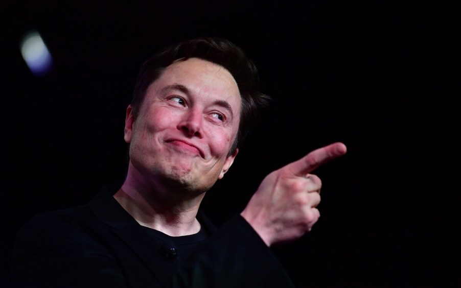 CEO Elon Musk makes a gesture at a Tesla in either California HQ2 or the Texas HQ.