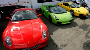 A red and yellow Ferrari are parked on either side of a bright green Lamborghini convertible at a supercar driving event.