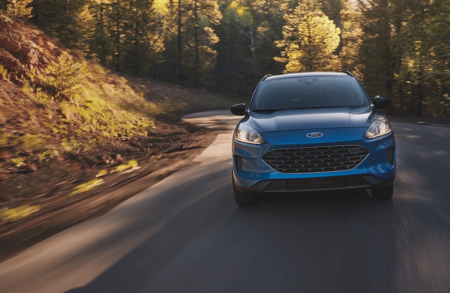 A blue Ford Escape driving down a wooded area, which is the Ford with the lowest insurance cost.