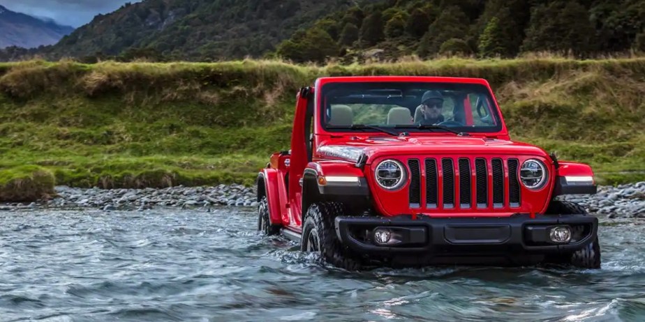 A red Jeep Wrangler small SUV is wading through water. 