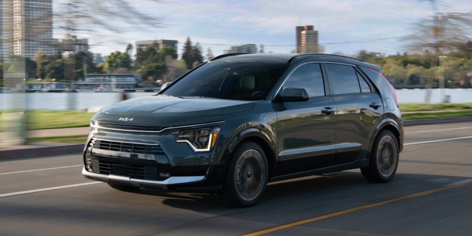 A black 2023 Kia Niro subcompact hybrid SUV is driving on the road. 