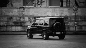 Black and white photo of a G-Class Wagon Mercedes SUV parked facing away from the camera, a brick wall visible in the background.