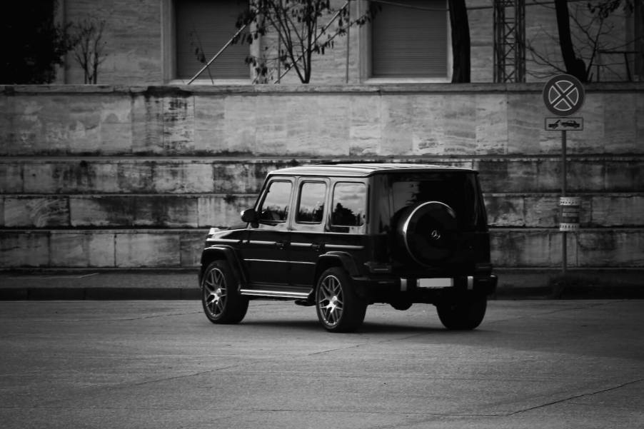 Black and white photo of a G-Class Wagon Mercedes SUV parked facing away from the camera, a brick wall visible in the background.