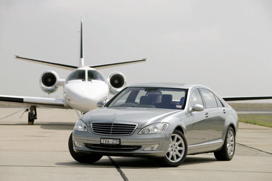 A used silver Mercedes-Benz S-Class luxury car poses in front of a private jet airplane.