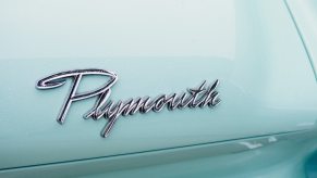 Chrome Plymouth brand logo on the trunk of an aqua-colored classic car.