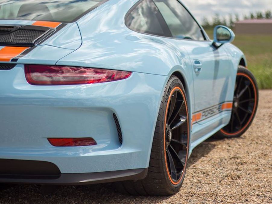 The rear fender of a powder blue porsche wearing the marigold orange stripes of Gulf Oil racing liveries as a tribute to the 917 that ran at Le Mans.