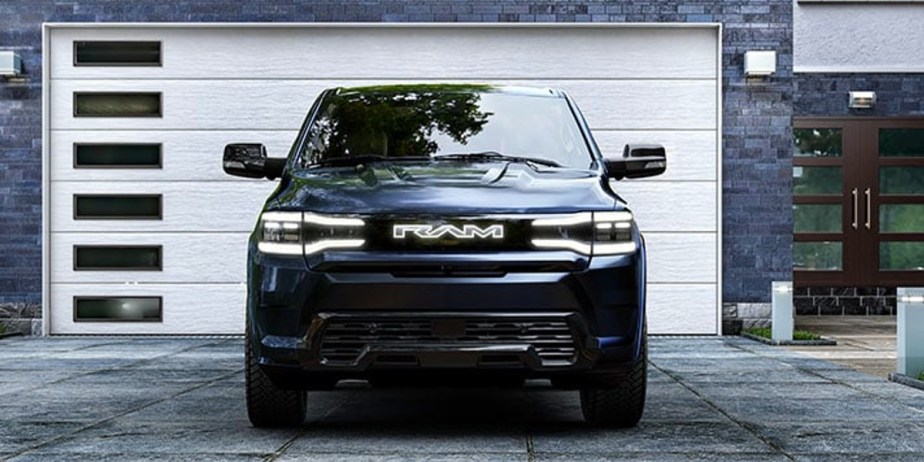 A blue 2025 Ram 1500 REV electric truck is parked in front of a garage.