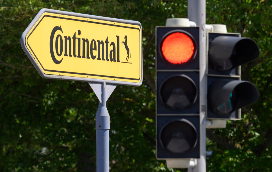 A red traffic light on a traffic light shines next to a sign pointing the way to the Continental plant.