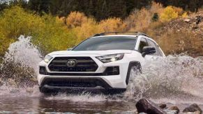 A white 2023 Toyota RAV4 small SUV is driving through a puddle.